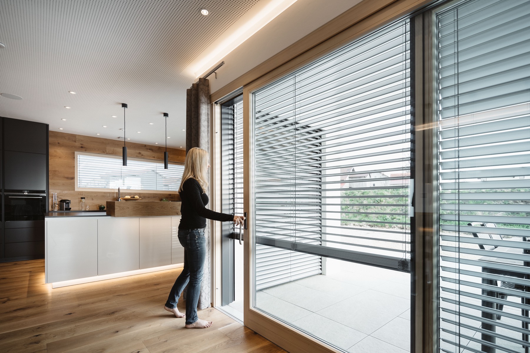Bright open living space with pendant lights and a floor-to-ceiling glass wall shaded by automatic blinds