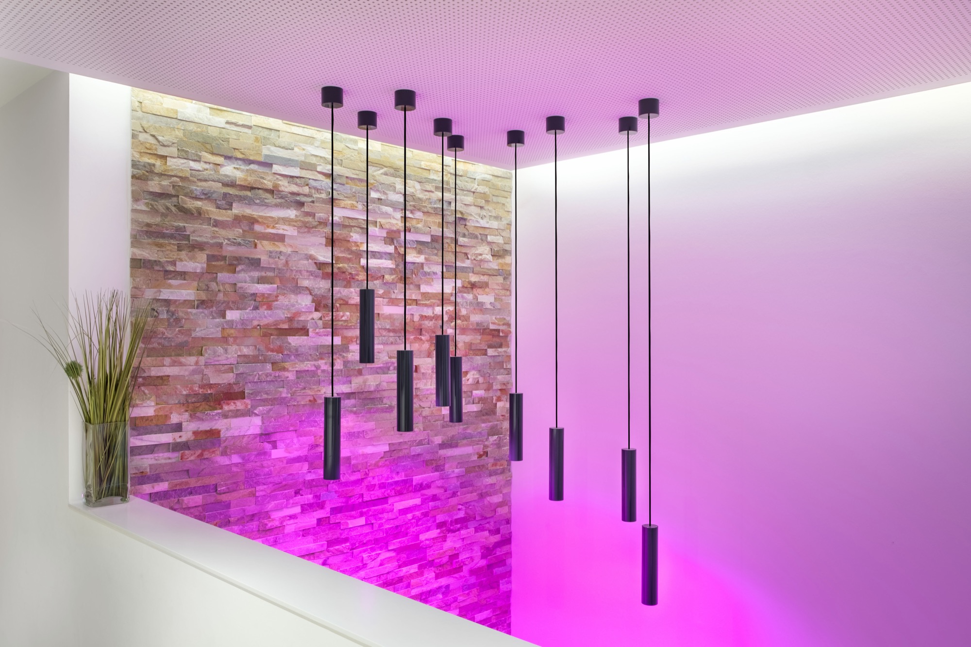 Nine slim pendant lights against a natural stone wall in a vivid lighting scene