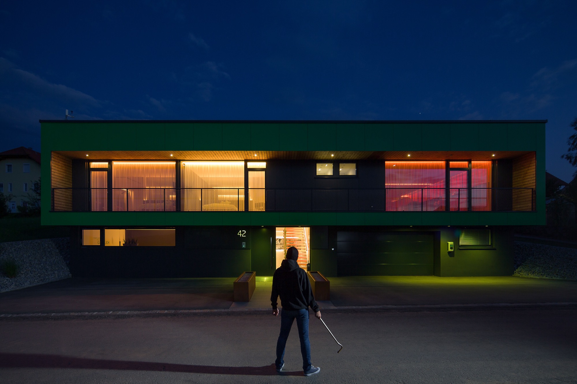 Modern home at night with warm windows and one room glowing red in an alert scene