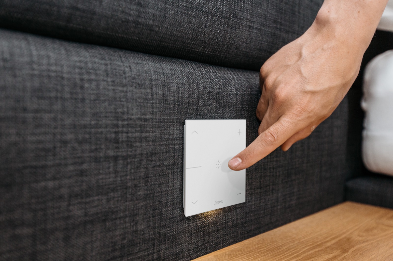 Hand reaching for a flush white Loxone switch set into an upholstered bed frame