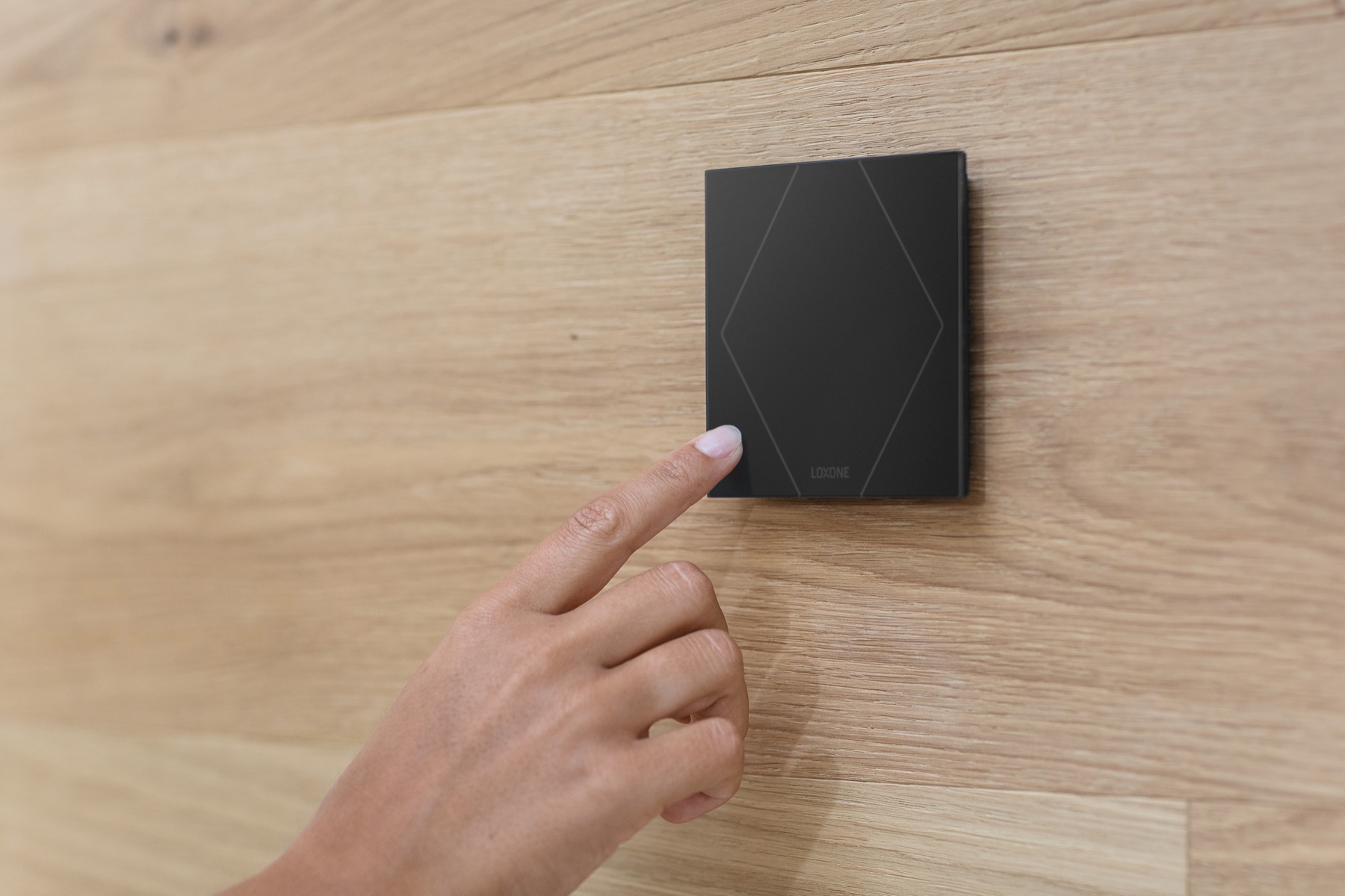 Finger touching a black Loxone Touch Pure switch set into an oak wall